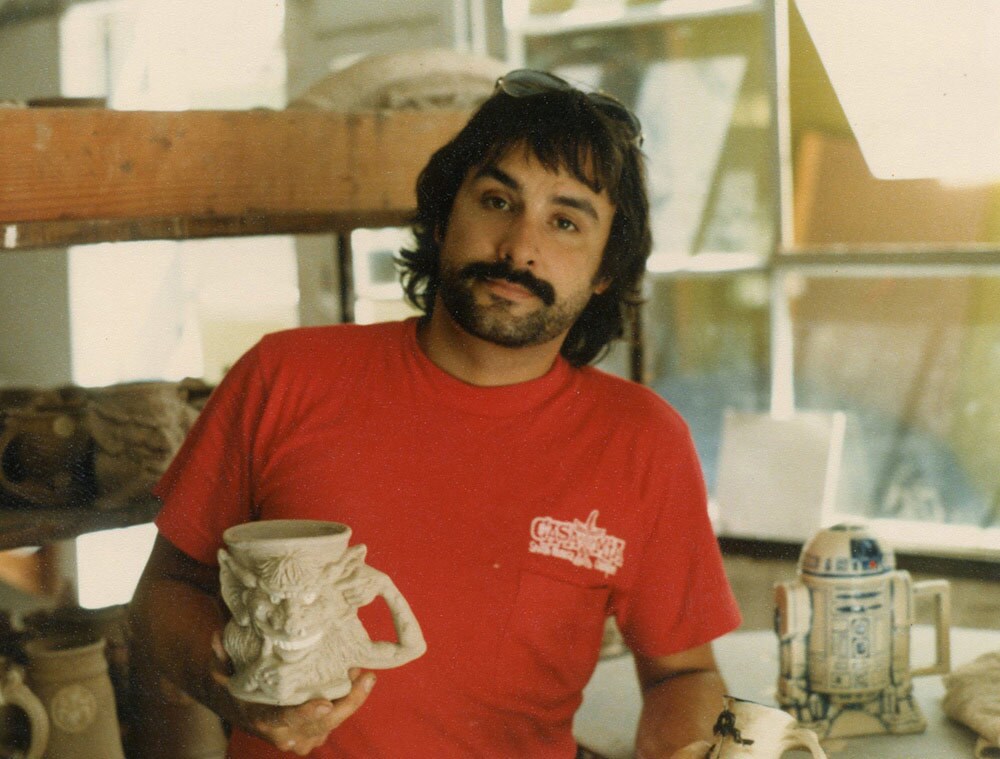 Pottery sculptor Jim Rumph holds one of his creature mugs. Behind him sits a fully painted R2-D2 tankard.
