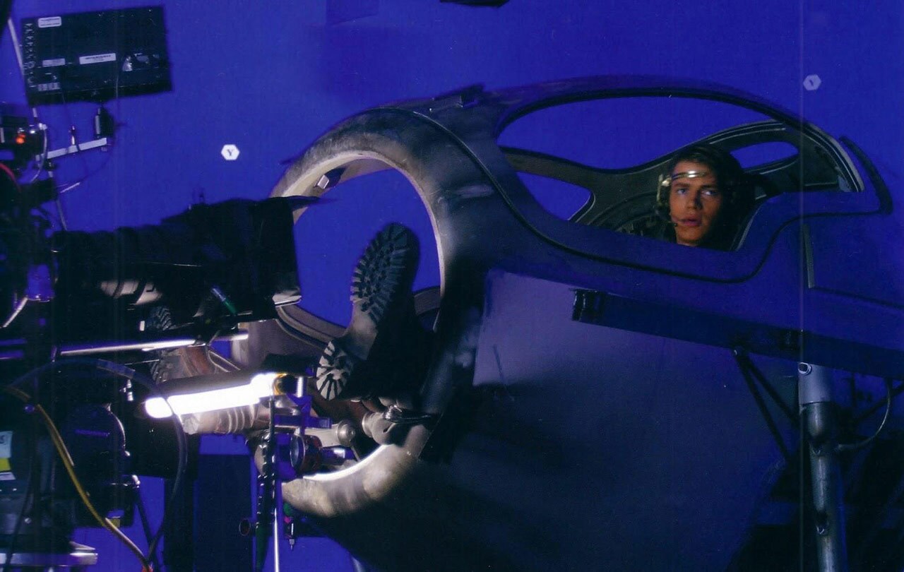 A behind-the-scenes bluescreen studio shot from Star Wars: Revenge of the Sith shows how characters had to dangle their legs outside of the cockpit to keep their knees out of the shot when filming atmospheric battle sequences.