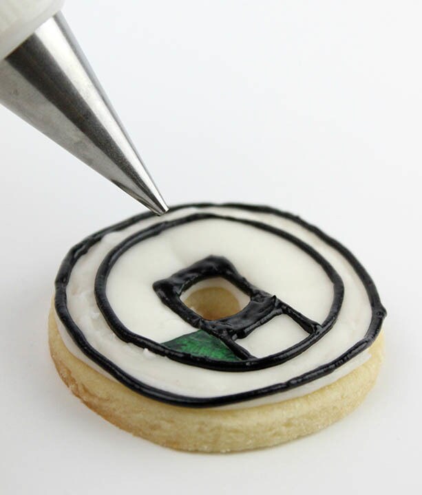 Black icing is piped onto the wheel element of a D-O cookie.