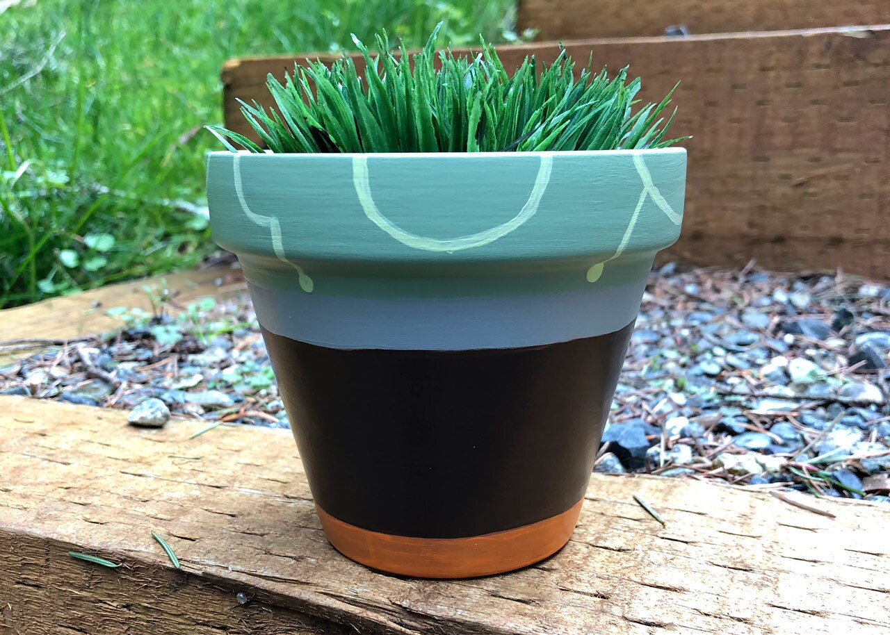 A terracotta pot painted blue, orange, and black for a Star Wars themed with a plant in it.