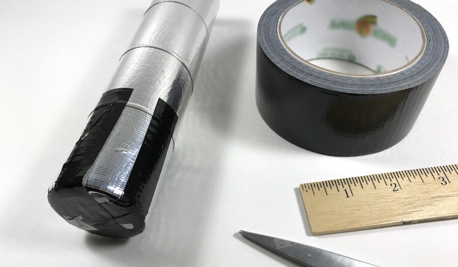 A vase wrapped in duct tape to resemble a lightsaber, next to a roll of black duct tape and a wooden ruler.