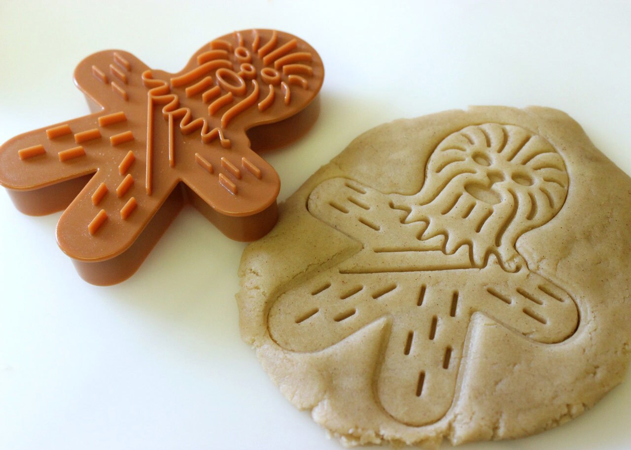 A cookie cutter in the shape of a Wookiee lies next to cookie dough with the cutter's imprint.