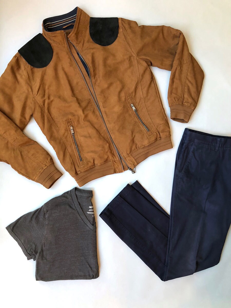 The clothes needed for a do-it-yourself Han Solo wardrobe include a brown suede bomber jacket, charcoal gray v-neck tee, and navy pants.