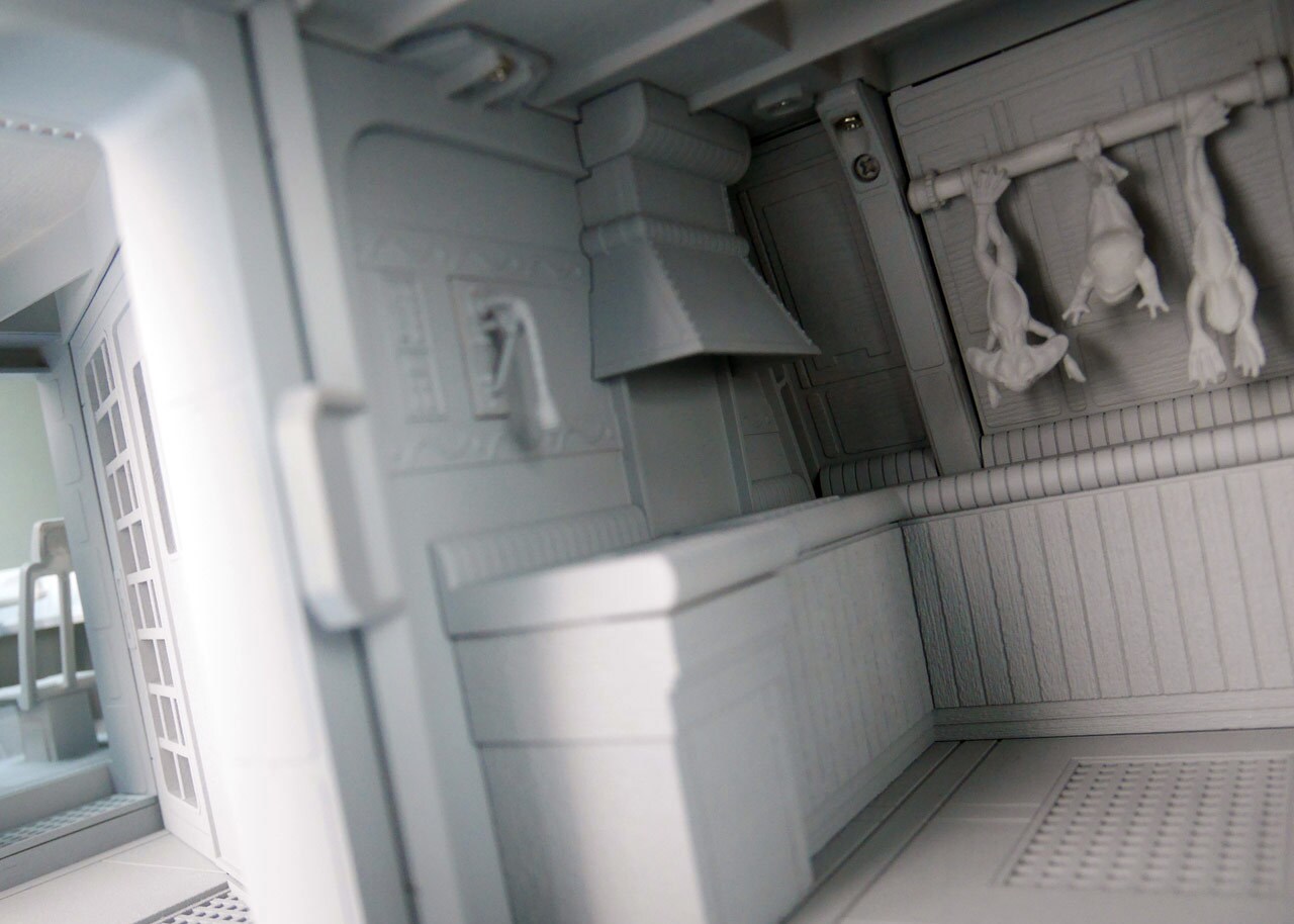 An unpainted 3D model of a kitchen used in designing the Jabba's Sail Barge toy vehicle created by Hasbro. Three amphibious creatures hang upside down from a rack against one of the walls.