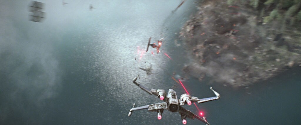 An X-wing shoots a TIE-Fighter above a body of water.