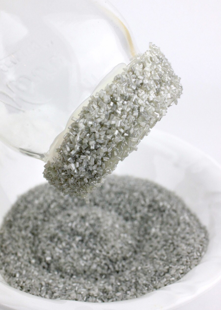 A mason jar rimmed with silver sugar for DIY thala-siren milkshakes, over a bowl full of silver sugar.