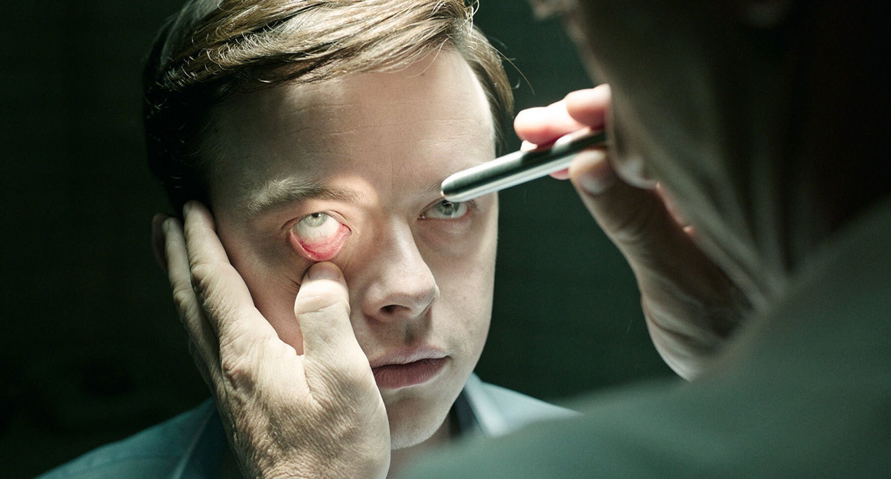 Actor Jason Isaacs (Volmer) examines Actor Dane DeHaan (Lockhart) eyes in the film "A Cure for Wellness"