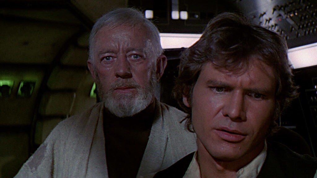 Obi-Wan Kenobi stands behind Han Solo at the controls of the Millennium Falcon in A New Hope.