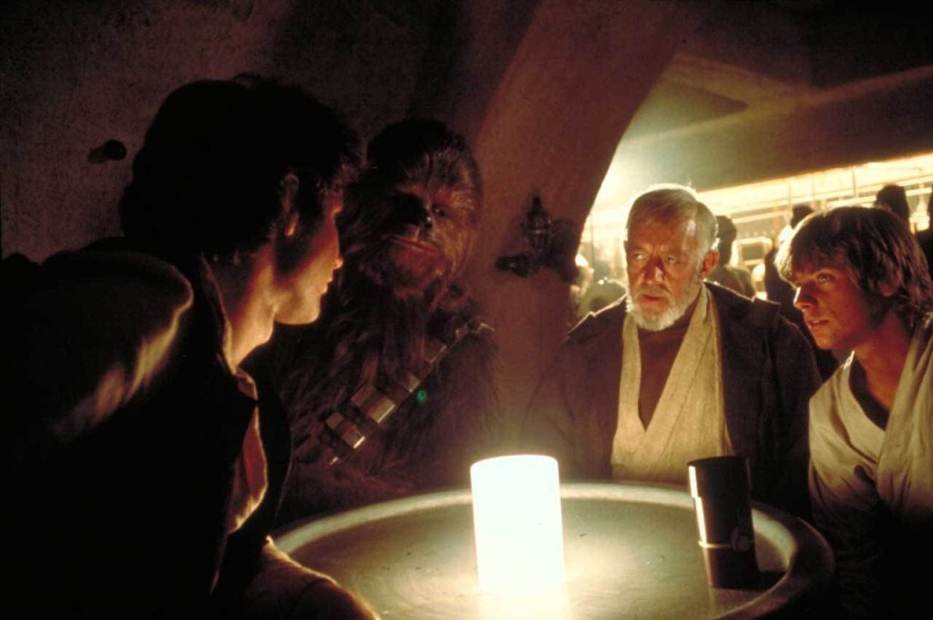 Luke Skywalker, Obi-Wan Kenobi, Chewbacca, and Han Solo sit at table in the Mos Eisley Cantina in A New Hope.