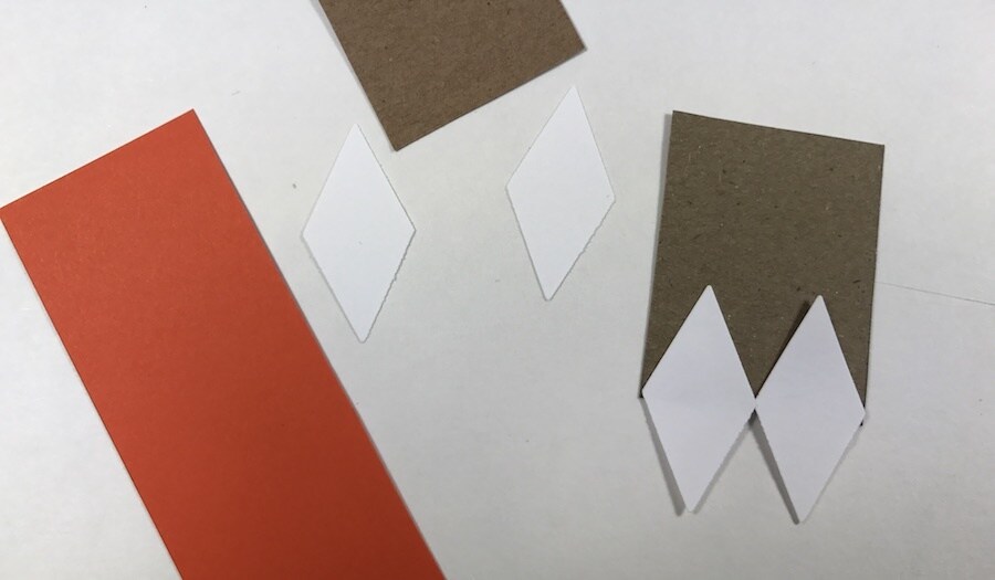 White paper diamonds glued to brown paper, beside orange cardstock.