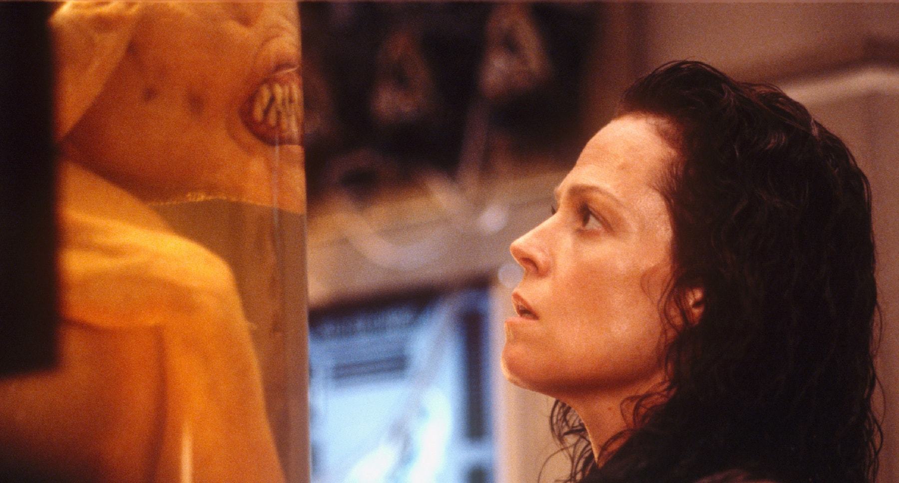 Actor Sigourney Weaver (as Ripley) staring at an alien in a tube in the film "Alien: Resurrection"