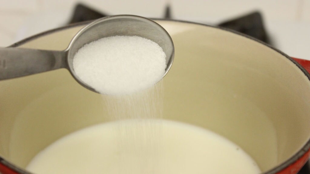 A tablespoon of sugar is poured into a saucepan.