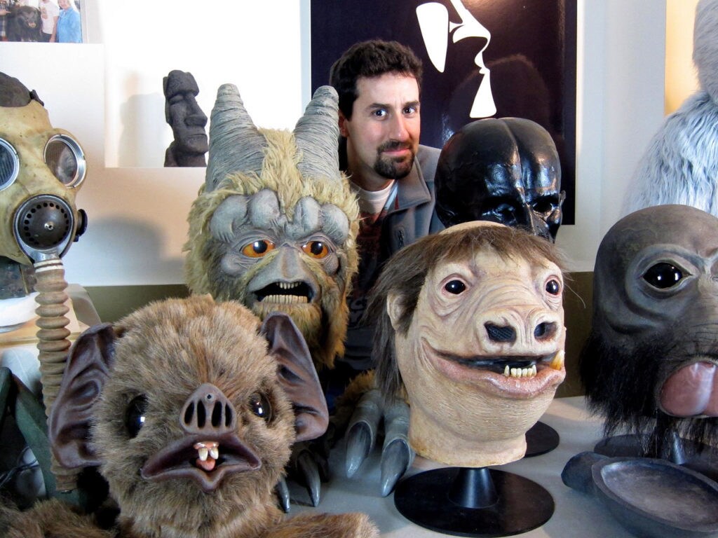 Visual artist Tom Spina poses with creature masks made by his company.