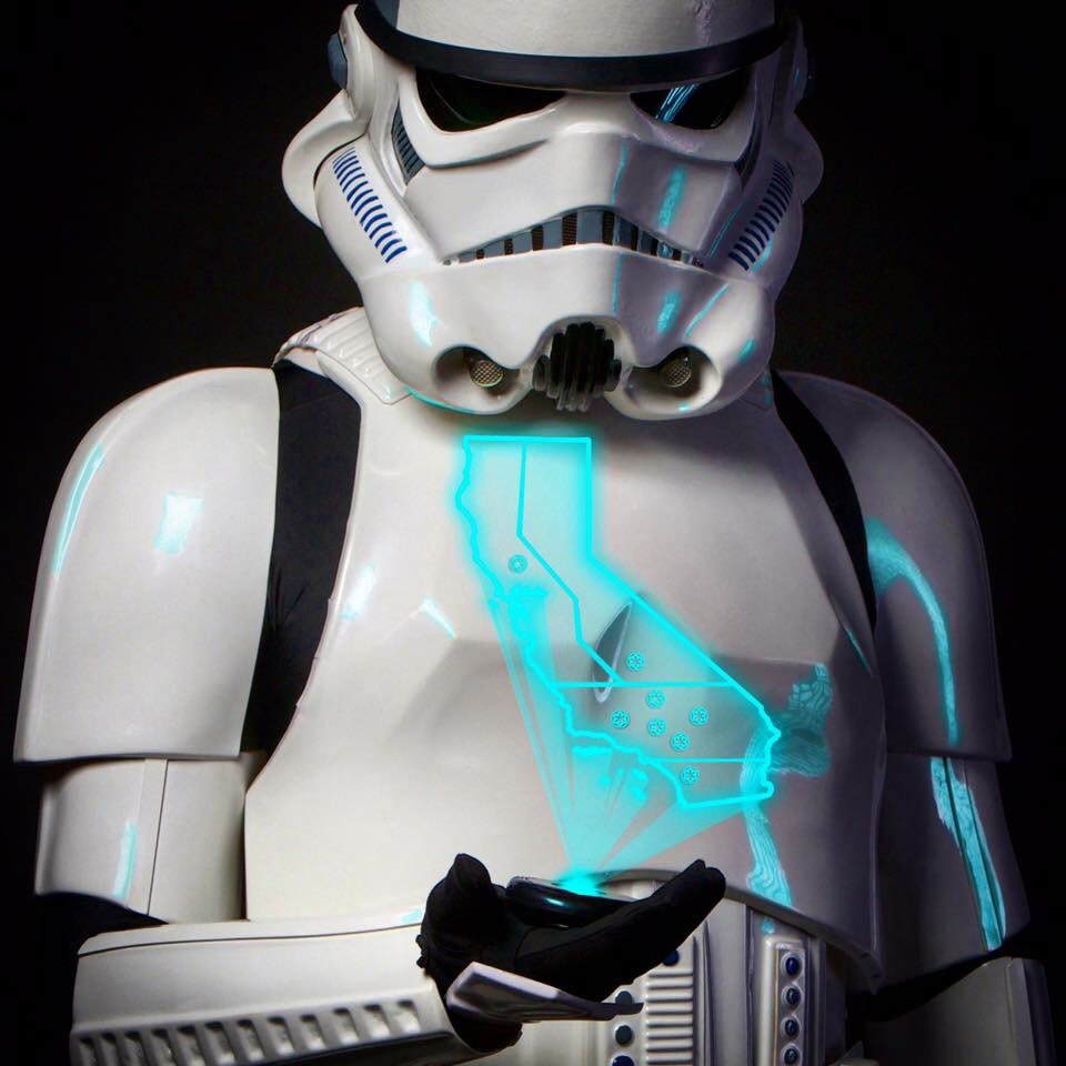 A stormtrooper holds a holographic projector in the palm of his hand that emits a blue, glowing light in the geographical shape of California.