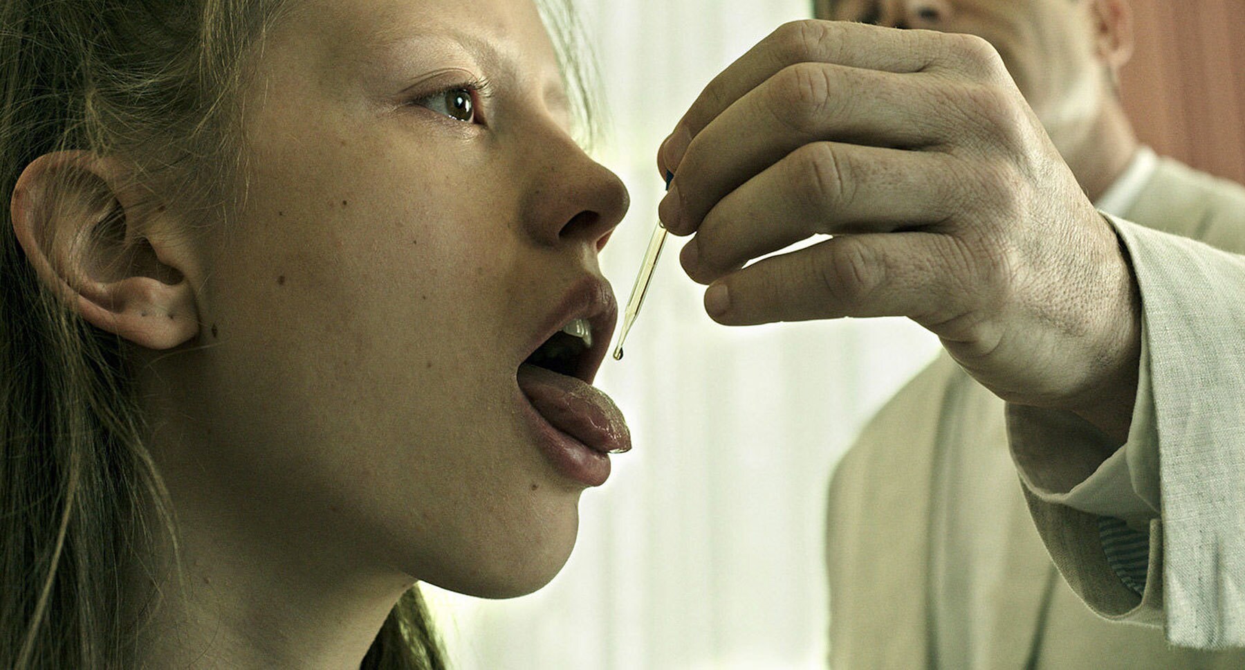Actor Jason Isaacs (as Volmer) gives Actor Mia Goth (as Hannah) medicine through a dropper in the film "A Cure for Wellness"