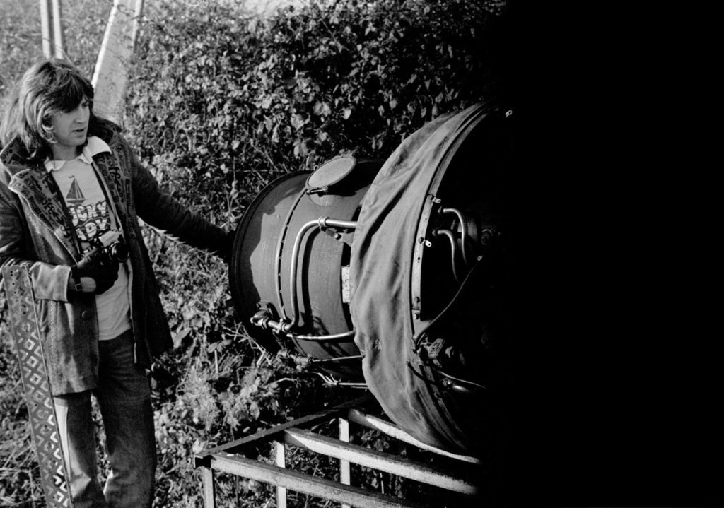 Roger Christian, set decorator for A New Hope, carries a camera while examining airplane scrap for use on set.