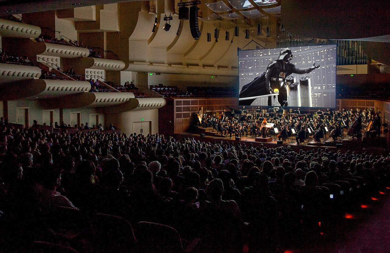 A full theatre audience listens to the San Francisco Orchestra perform the score from Star Wars: The Empire Strikes Back alongside a screen playing the movie.