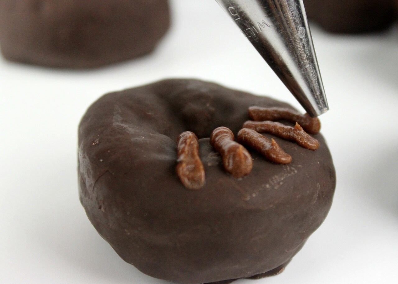 Brown icing is piped onto dark chocolate mini donuts.