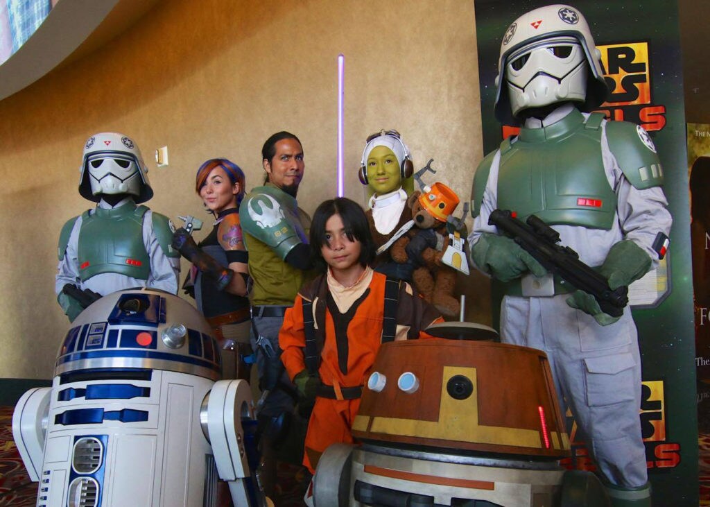 A group of fans in costume as the Rebels characters pose with R2-D2 and Chopper.