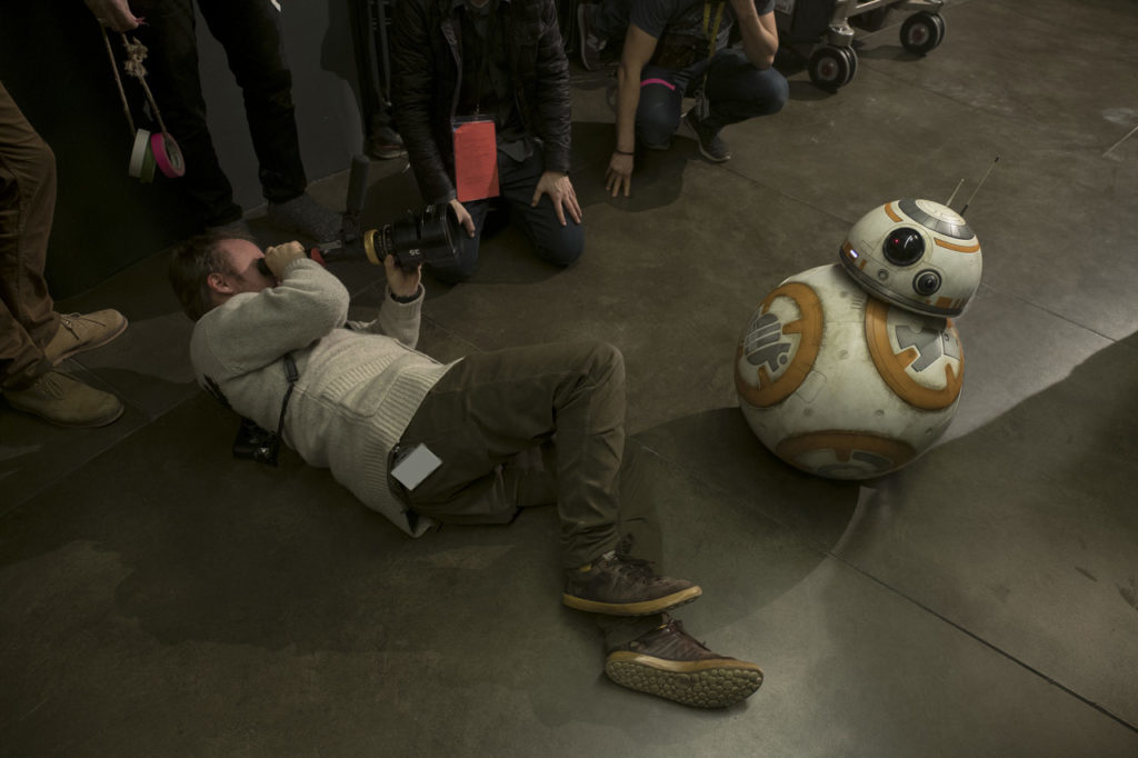 Director Rian Johnson lies on his side as he focuses his viewfinder on BB-8 in a behind-the-scenes photo from the making of The Last Jedi.