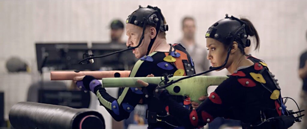 Janina Gavankar wears motion-capture gear while holding a prop gun.