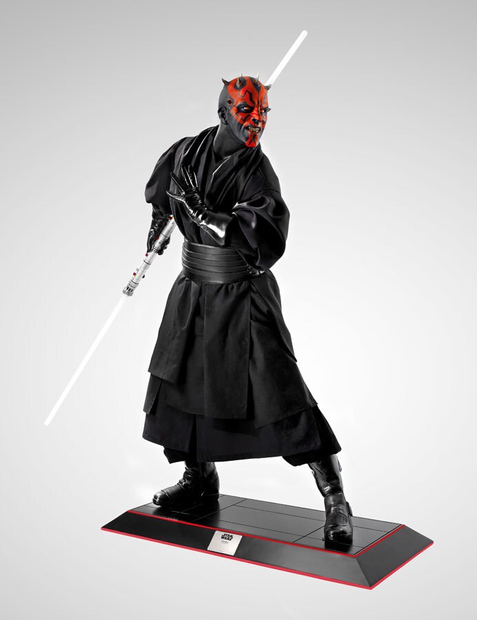 Statue of Darth Maul dressed in a black cloak with a dual-edged light saber.