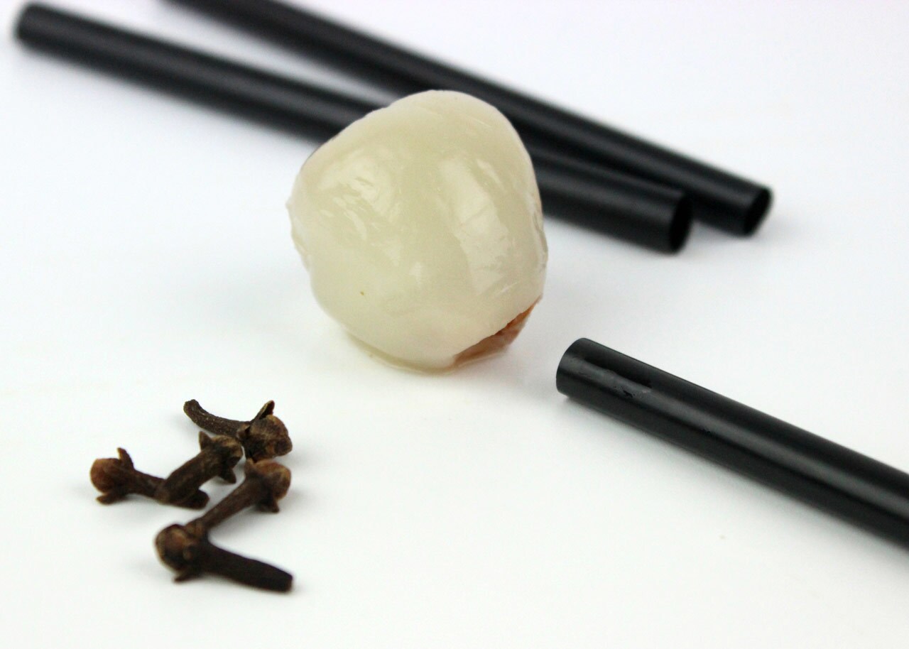 A peeled lychee fruit next to black straws and cloves.
