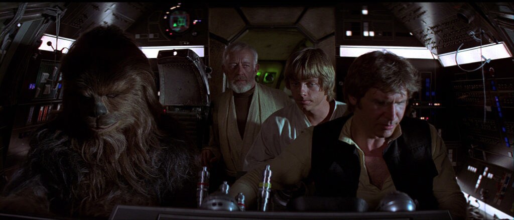 Han, Luke, Obi-Wan, and Chewie sit in the cockpit of the Millennium Falcon.
