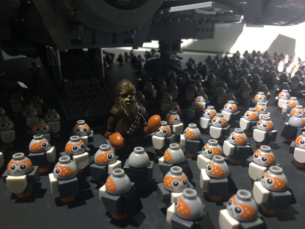 A Lego Chewbacca stands beneath a Lego Millennium Falcon surrounded by Lego porgs.