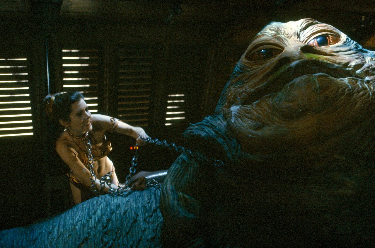 Princess Leia strangles Jabba the Hutt with a chain, while wearing her iconic golden bikini.