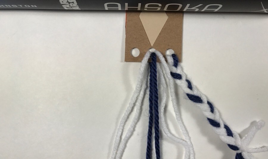 White and blue yarn threaded through holes in a cardboard bookmark.