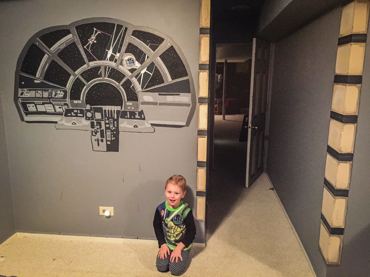 A child kneels next to a wall decal that looks like the view from the Millennium Falcon cockpit.