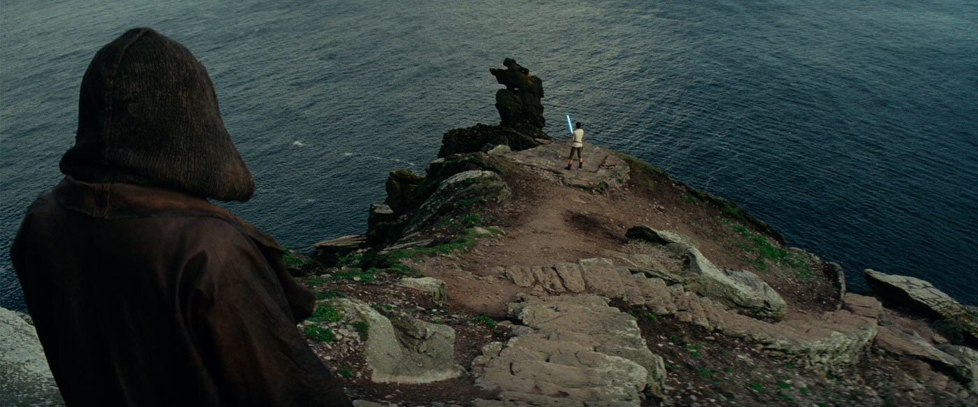 Luke looks on as Rey practices with her a lightsaber on a cliff.