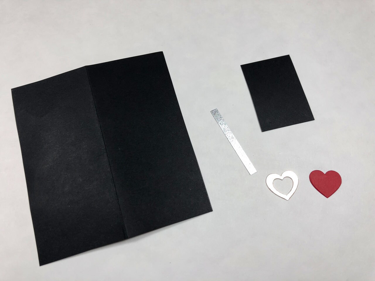 Pieces of black card stock, a strip of silver paper, and red and gold paper hearts. This is a Rose Tico-inspired Electro-Shock Prod Valentine's Day Card in progress.
