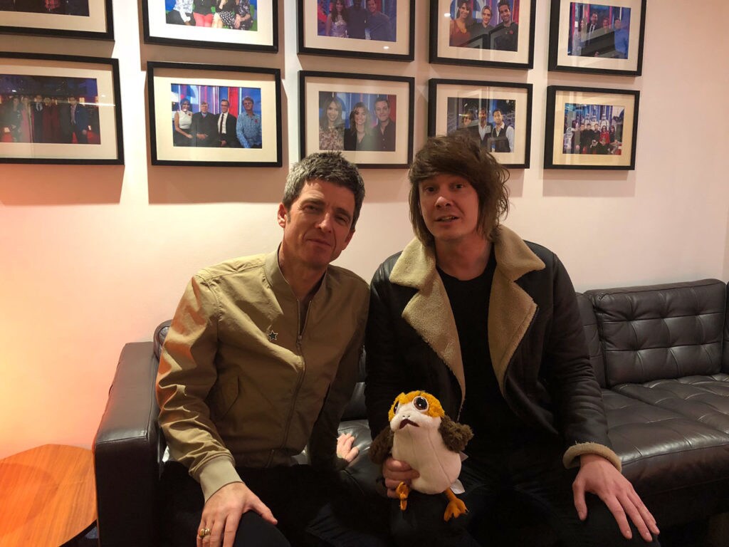 Noel Gallagher and Jamie Stangroom on a couch with a plush toy porg,