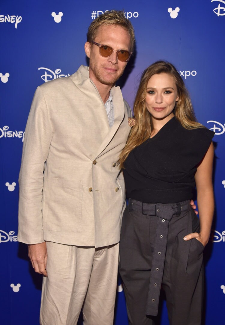 Elizabeth Olsen and Paul Bettany are pictured at the D23 Expo against a blue background. 