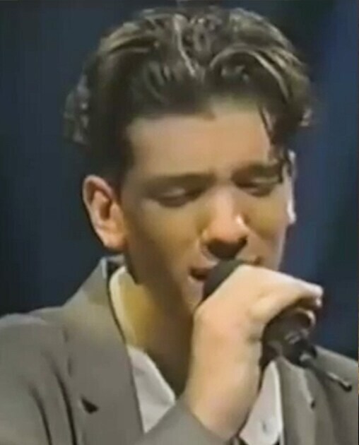 JC Chasez in tan jacket singing with a mic