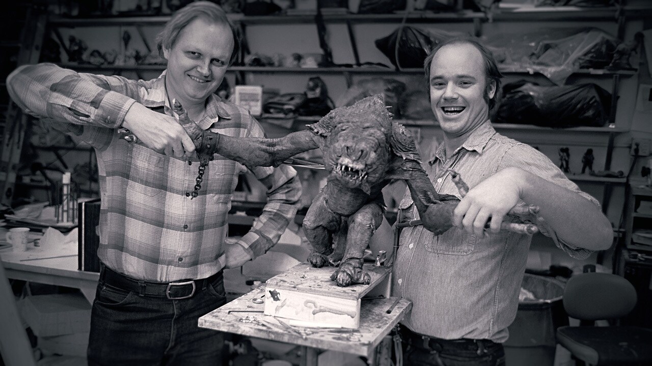 Phil Tippett and Dennis Muren holding hands with the rancor, smiling and like, shaking hands with the puppet.