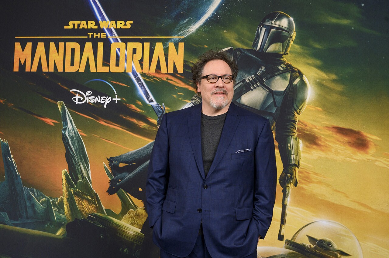 Jon Favreau in front of a Mandalorian Season 3 poster