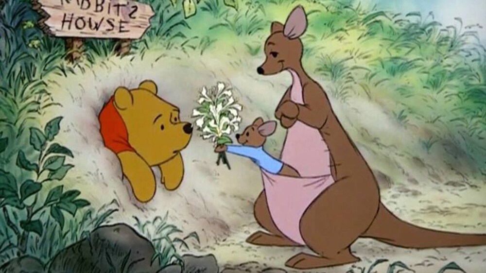 Roo in Kanga's pouch handing flowers to Winnie the Pooh
