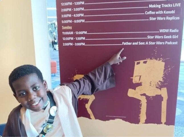 Keith points to a sign at Star Wars Celebration Anaheim 2022 showing the Podcast Stage schedule.