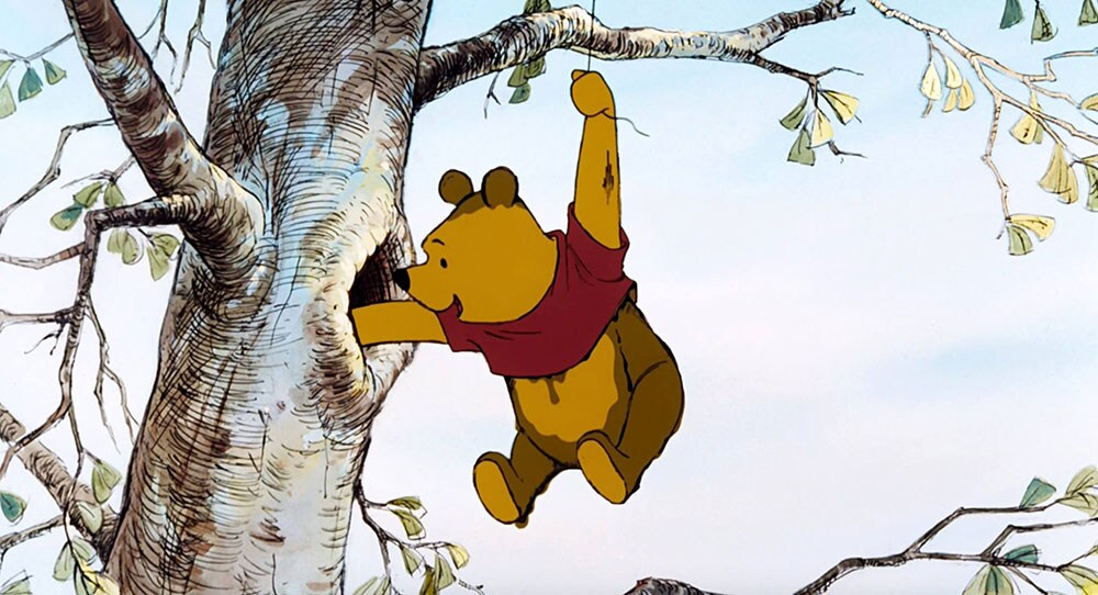 Winnie the Pooh hanging from a tree branch, reaching for something inside the tree