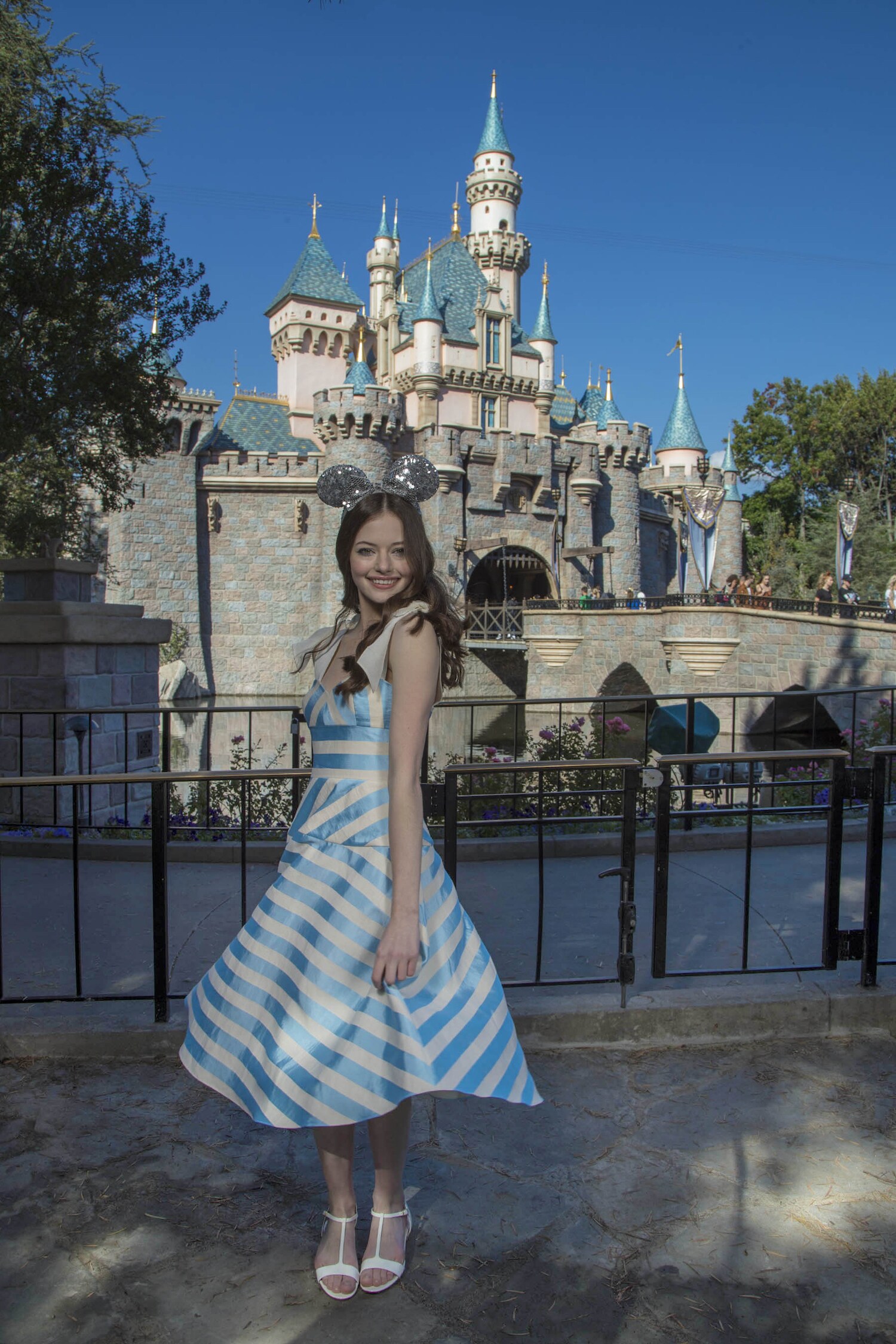 Mackenzie Foy in Blue and White striped dress posing in front of the Disneyland castle