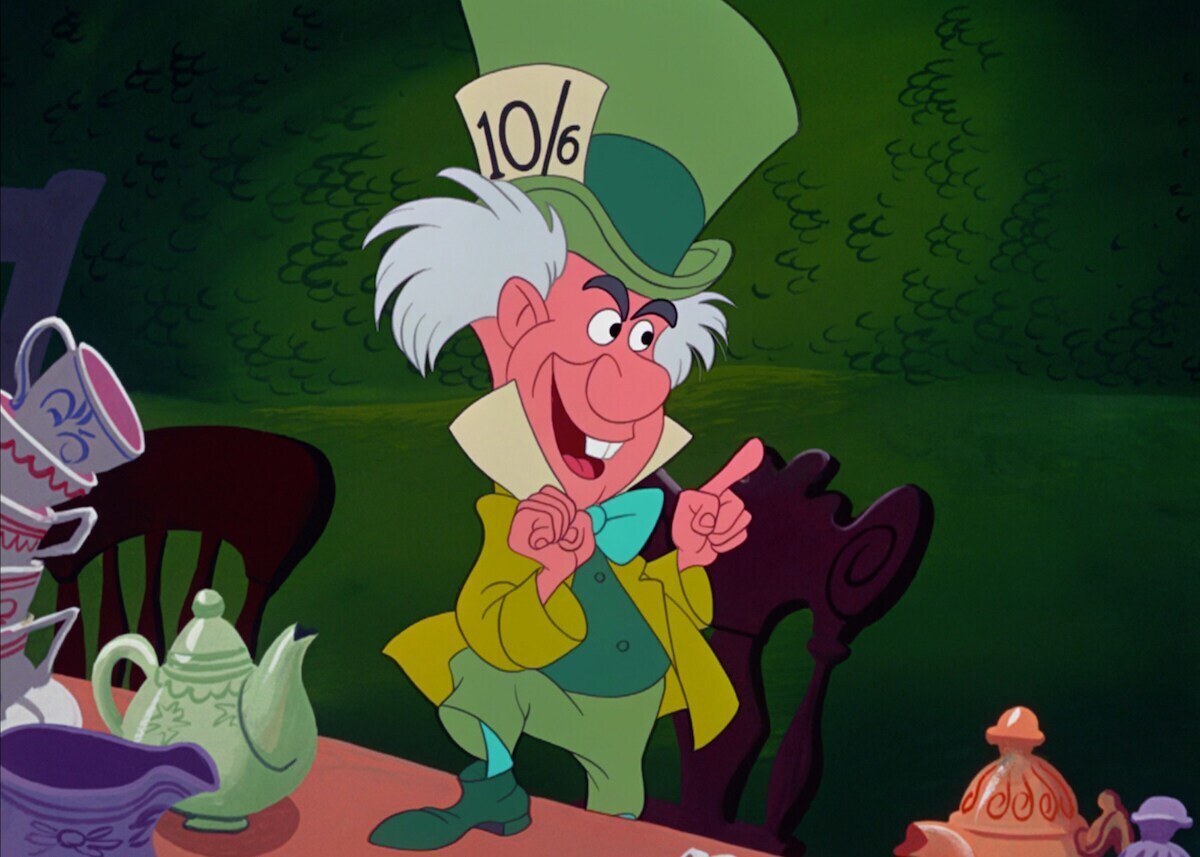 The Mad Hatter standing on a chair with one foot on the table in the animated movie "Alice in Wonderland"