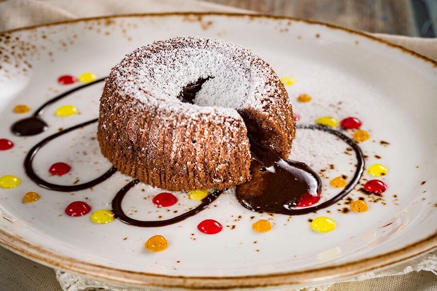 Image of oozing molten chocolate cake on a plate decorated with a chocolate swirl and dots of red, yellow, and orange