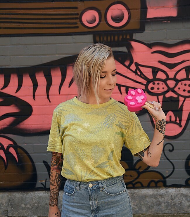 blonde woman holding a pink paw-sicle and wearing a yellow tee shirt with floral patterns