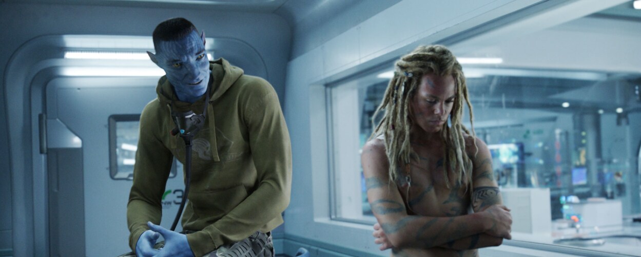 Colonel Quaritch, in recombinant form, talking to his son, Spider, who is turned away with crossed arms.