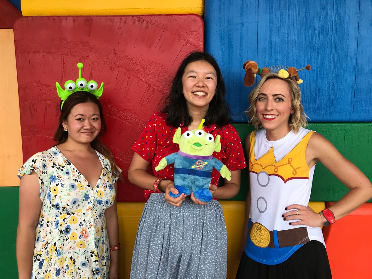 Oh My Disney Correspondents Jenny Tran, Kelly Lin, and Michelle Lema in front of a toy block wall in Toy Story Land in Walt Disney World