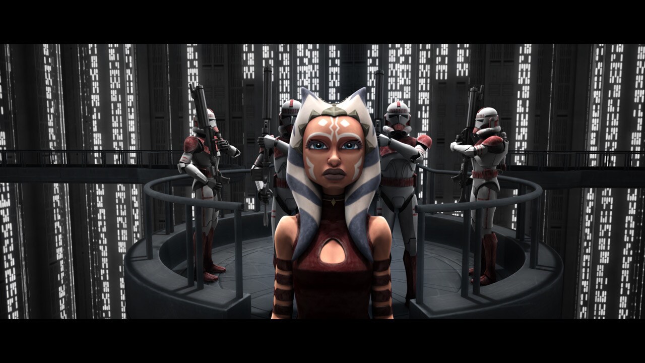 A manacled Ahsoka Tano is brought by clone troopers into the spacious military tribunal chamber. ...