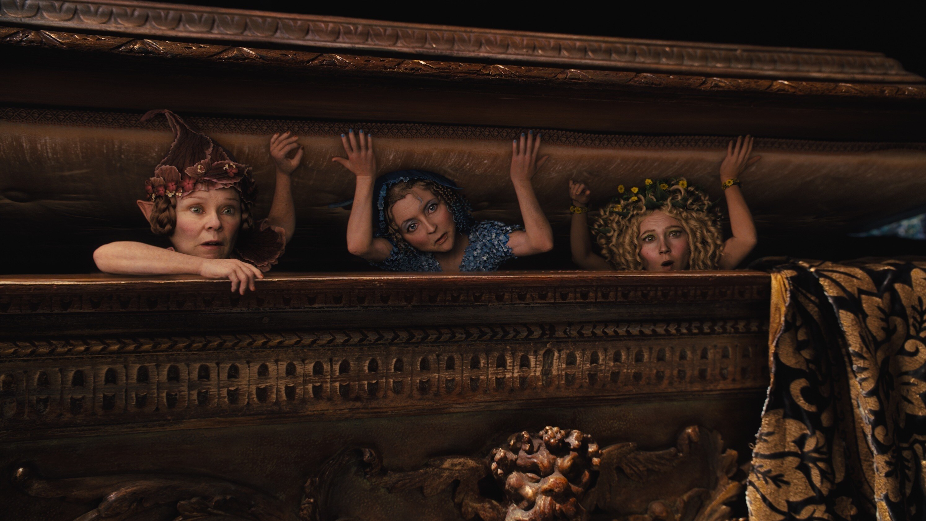 The three flower pixies, Knotgrass (played by Imelda Stauton), Flittle (played by Lesley Manville), and Thistlewhit (played by Juno Temple) peeking out of a box in the movie "Maleficent"